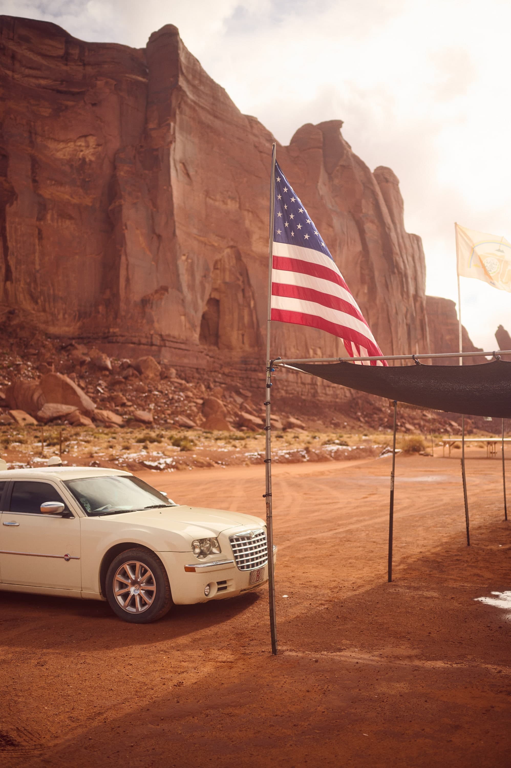 US-Flagge und weißer Chrysler vor einer roten Felswand im Monument Valley